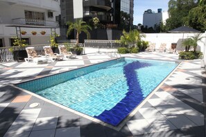 A swimming pool with tiled flooring, surrounded by lounge chairs and potted plants. - Bela Vista Hotel & Flat (Porto Alegre)