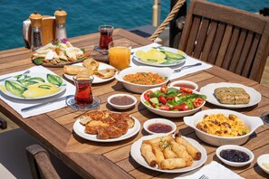 Une table en bois, dressée avec différents plats, notamment des salades, du pain et un bol de soupe.