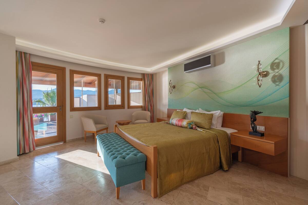 Ein geräumiges Schlafzimmer mit einem großen Bett, einer Bank, einem Schreibtisch und Blick ins Freie.