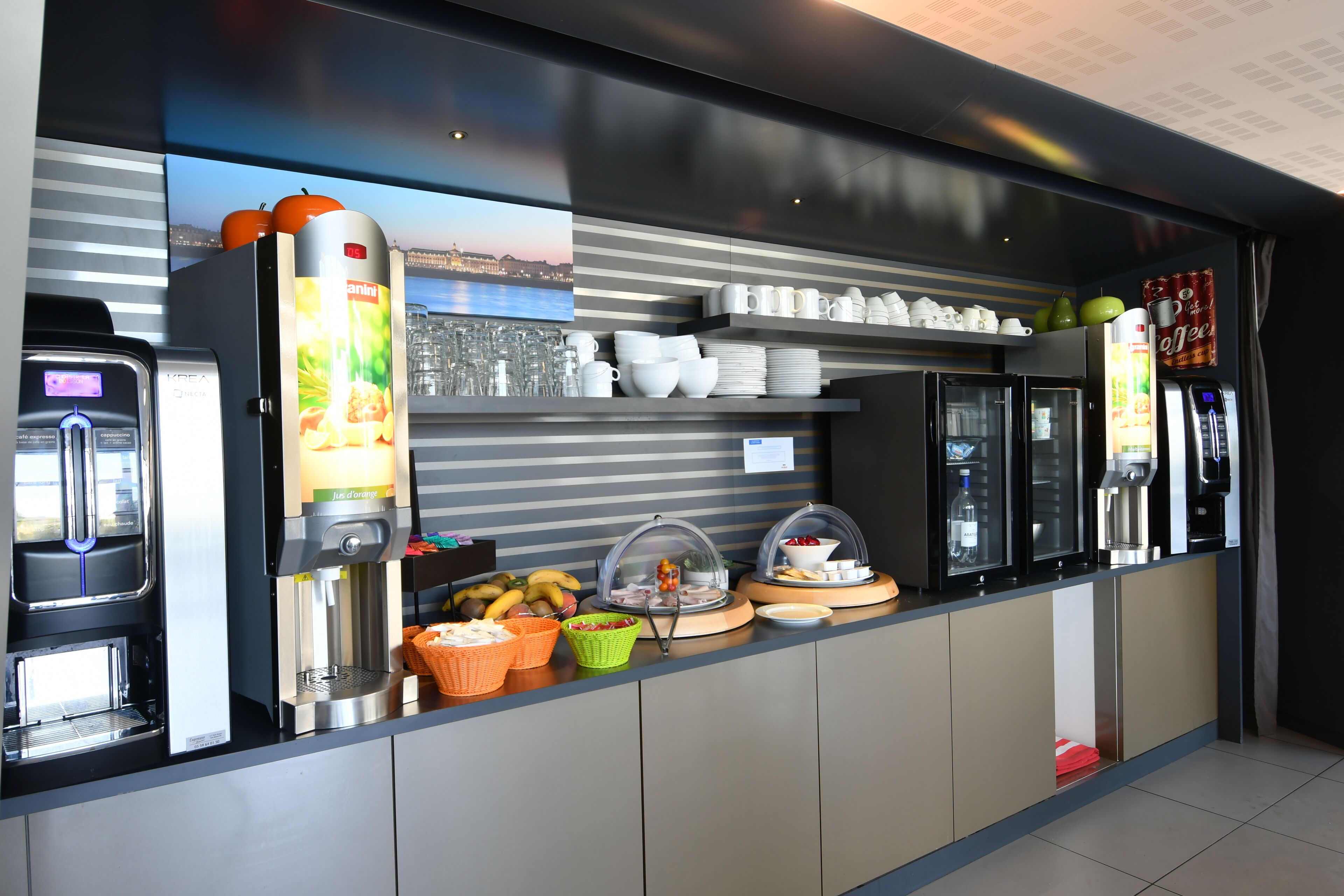 A self-service breakfast station with coffee machines, a fruit display, and a variety of breakfast items.