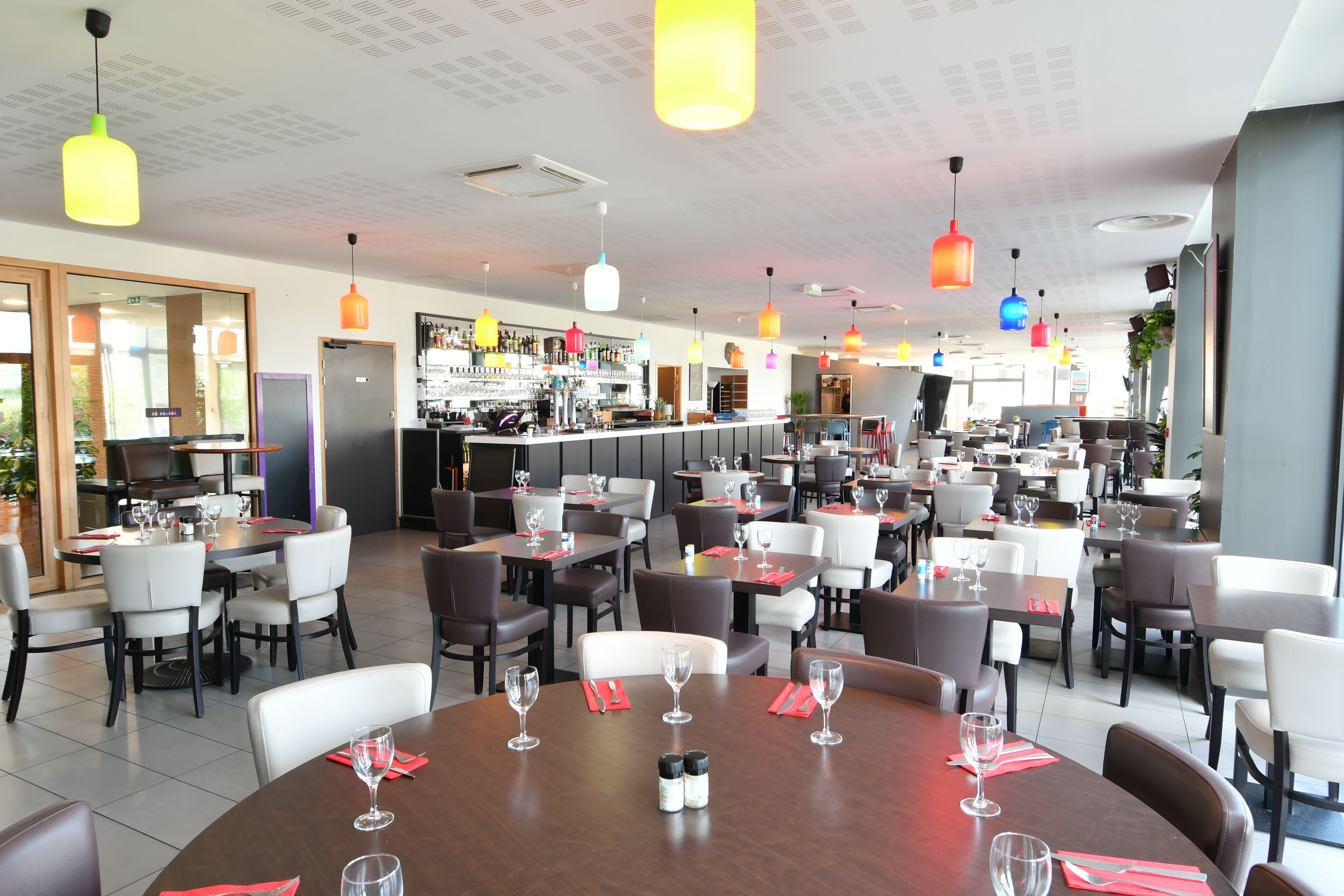 Un restaurant doté de nombreuses tables et chaises, d’un bar et d’un éclairage suspendu.