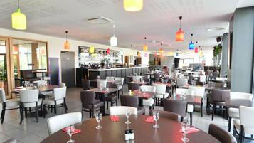 Un restaurant doté de nombreuses tables et chaises, d’un bar et d’un éclairage suspendu.