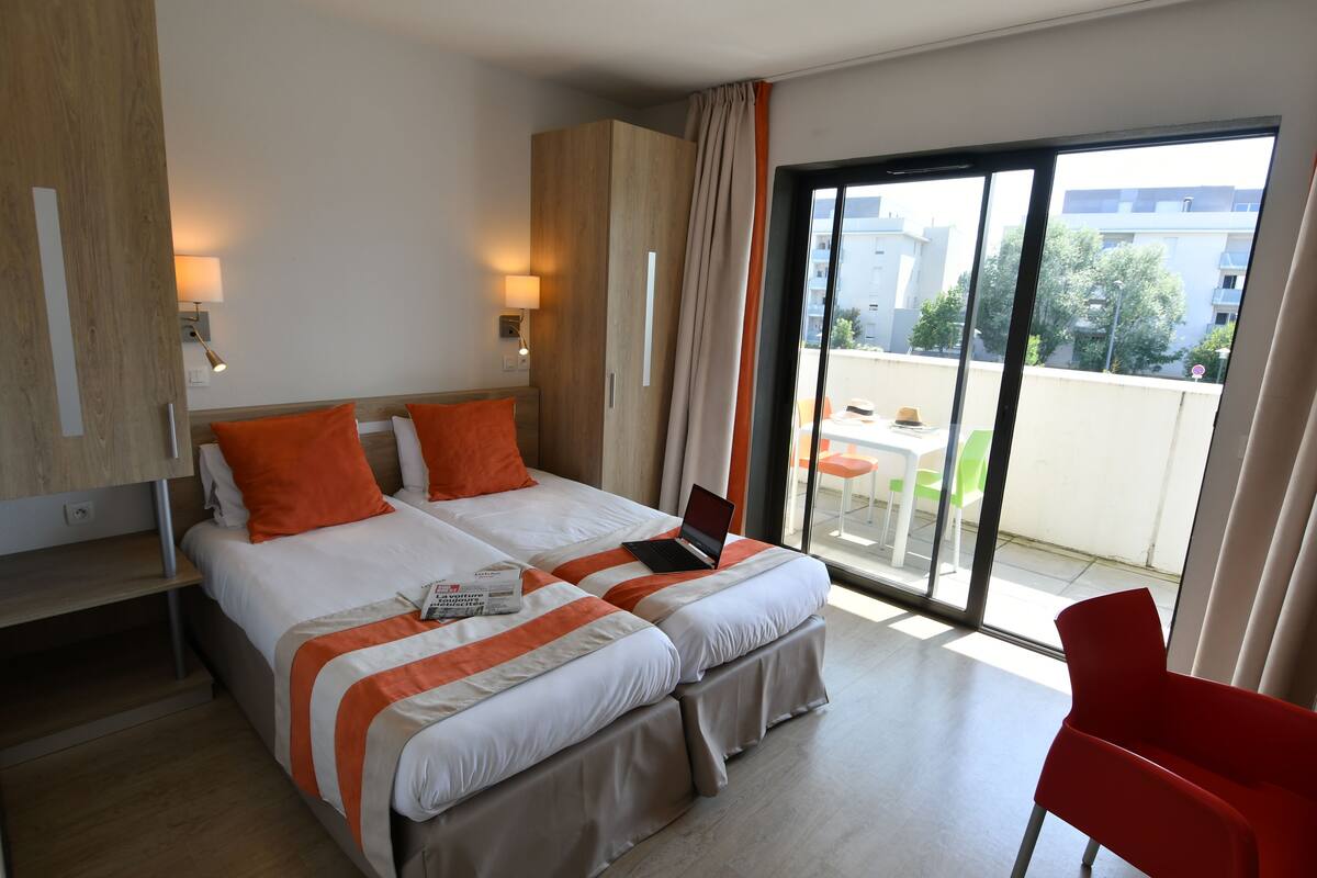 A hotel room with a large bed, a laptop, and a red chair.