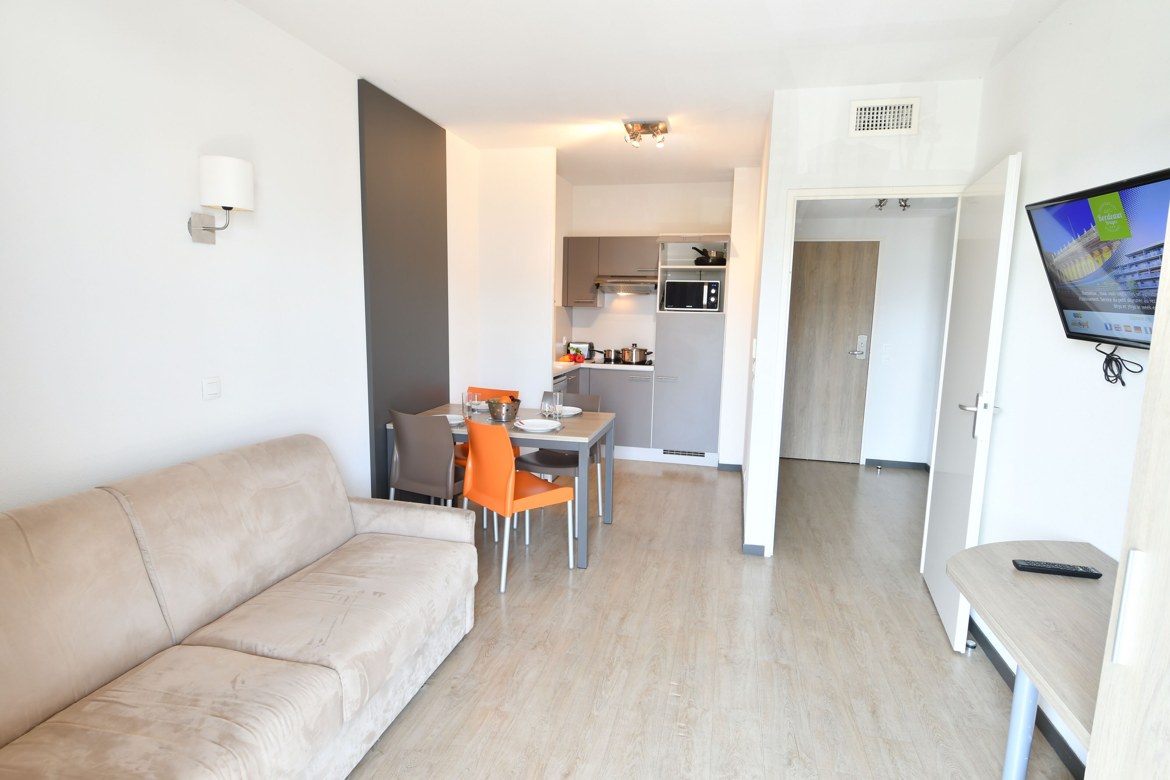 Un appartement moderne comprenant un salon, un coin repas, une kitchenette et un téléviseur fixé au mur.