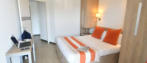 Hotellihuone, jossa on sänky, työpöytä kannettavalla tietokoneella ja vaatekaappi.