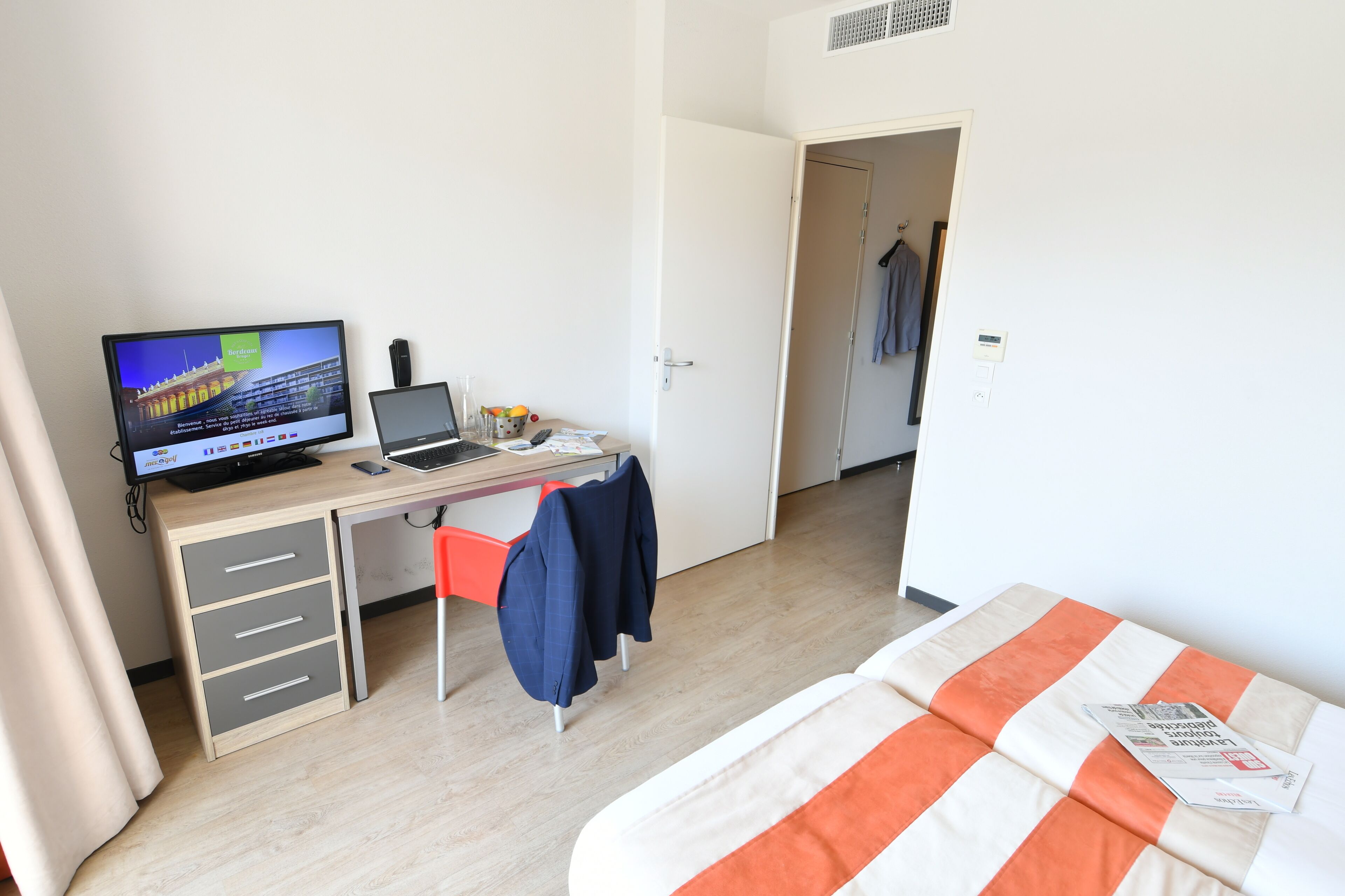 Una habitación de hotel con una cama, un escritorio con una computadora portátil, un televisor y una puerta que da a otra habitación.
