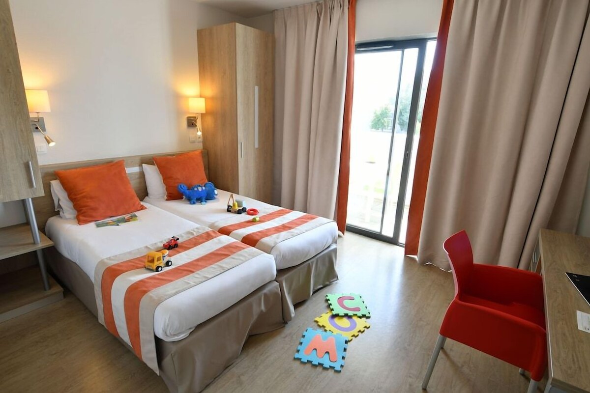 Una camera d'albergo con due letti, una scrivania e una sedia.