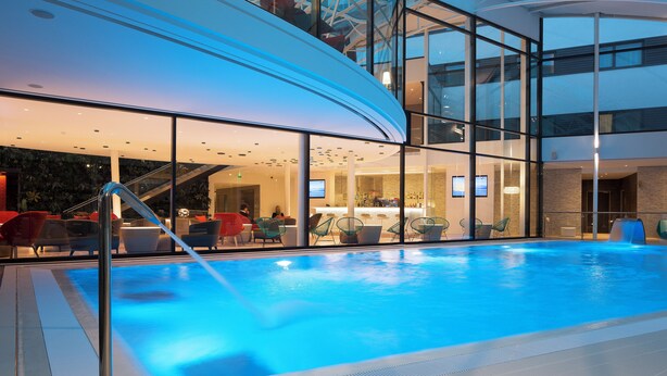 Une piscine intérieure avec des murs en verre, un bar et des sièges avec des chaises rouges.