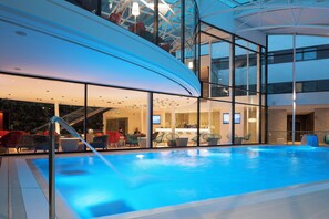 Ein Innenpool mit Glaswänden, einer Bar und roten Sitzgelegenheiten.