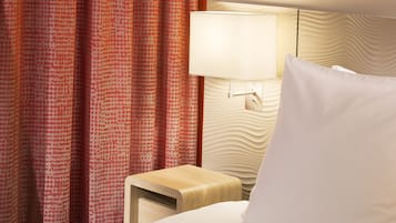 A hotel room with a bed, a nightstand, a lamp, and a patterned curtain.