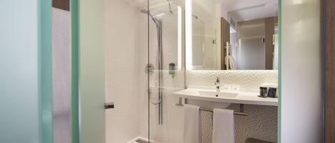 Un baño moderno con ducha de vidrio, un lavabo con espejo y un banco.