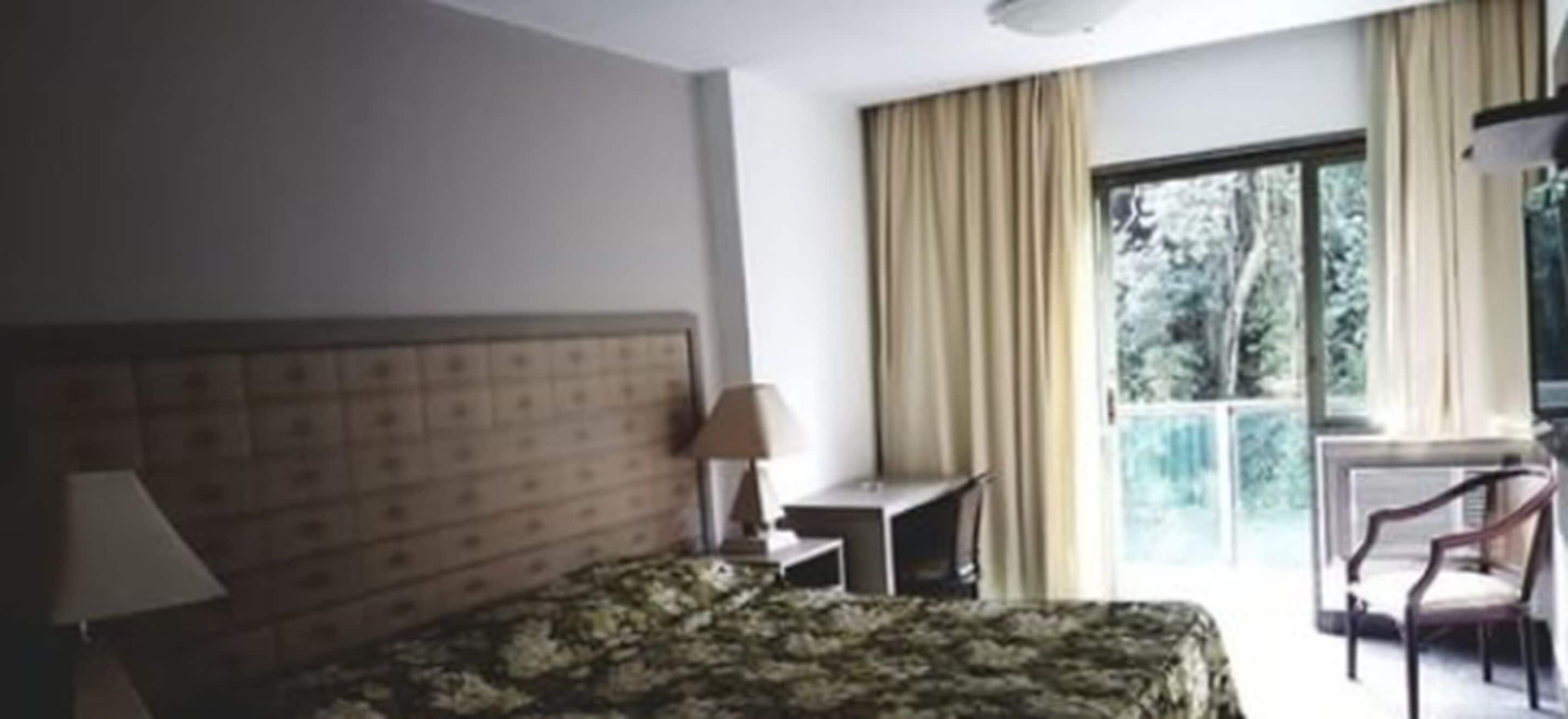 A hotel room with a bed, a desk, a chair, and a window with curtains.