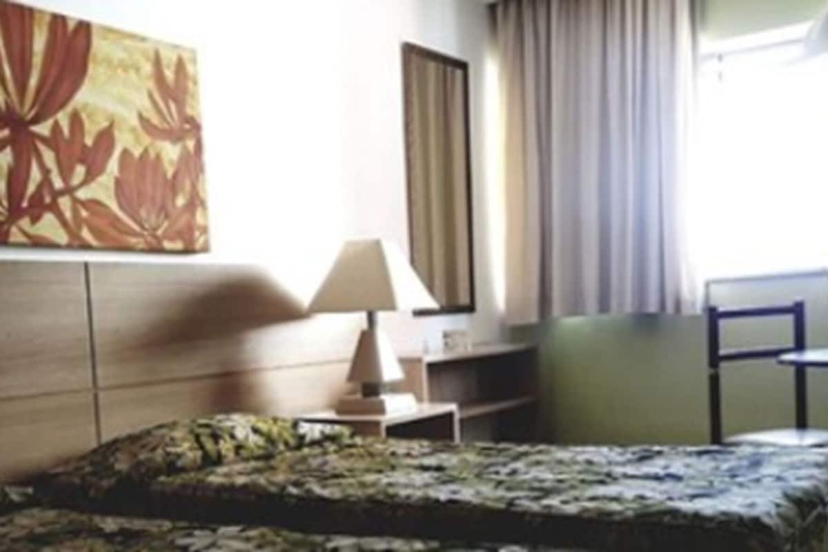 Ein Hotelzimmer mit Bett, Schreibtisch, Stuhl, Lampe und einem großen Blumenbild an der Wand.