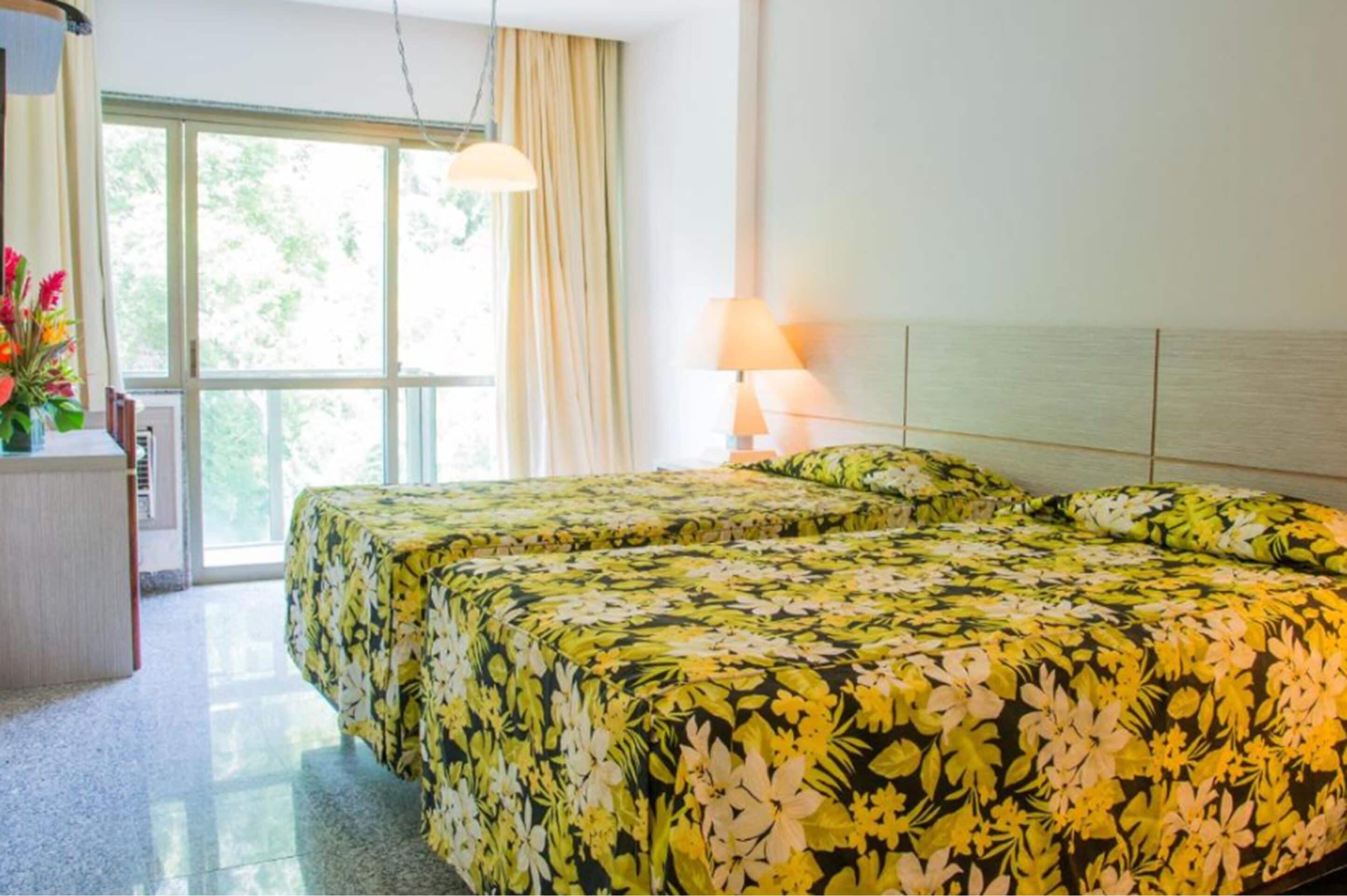 Habitación de hotel con dos camas, un escritorio y una ventana con cortinas.
