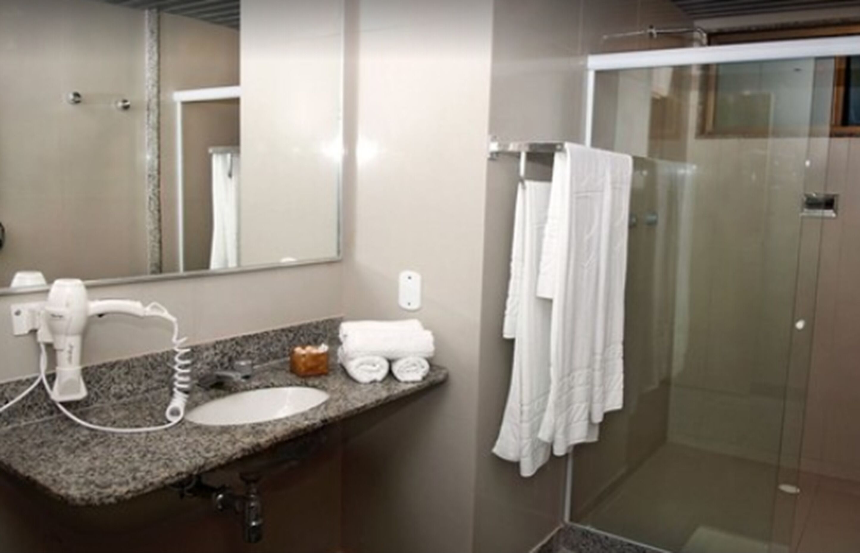 A bathroom with a granite countertop, a white sink, a hairdryer, and a glass-enclosed shower area.