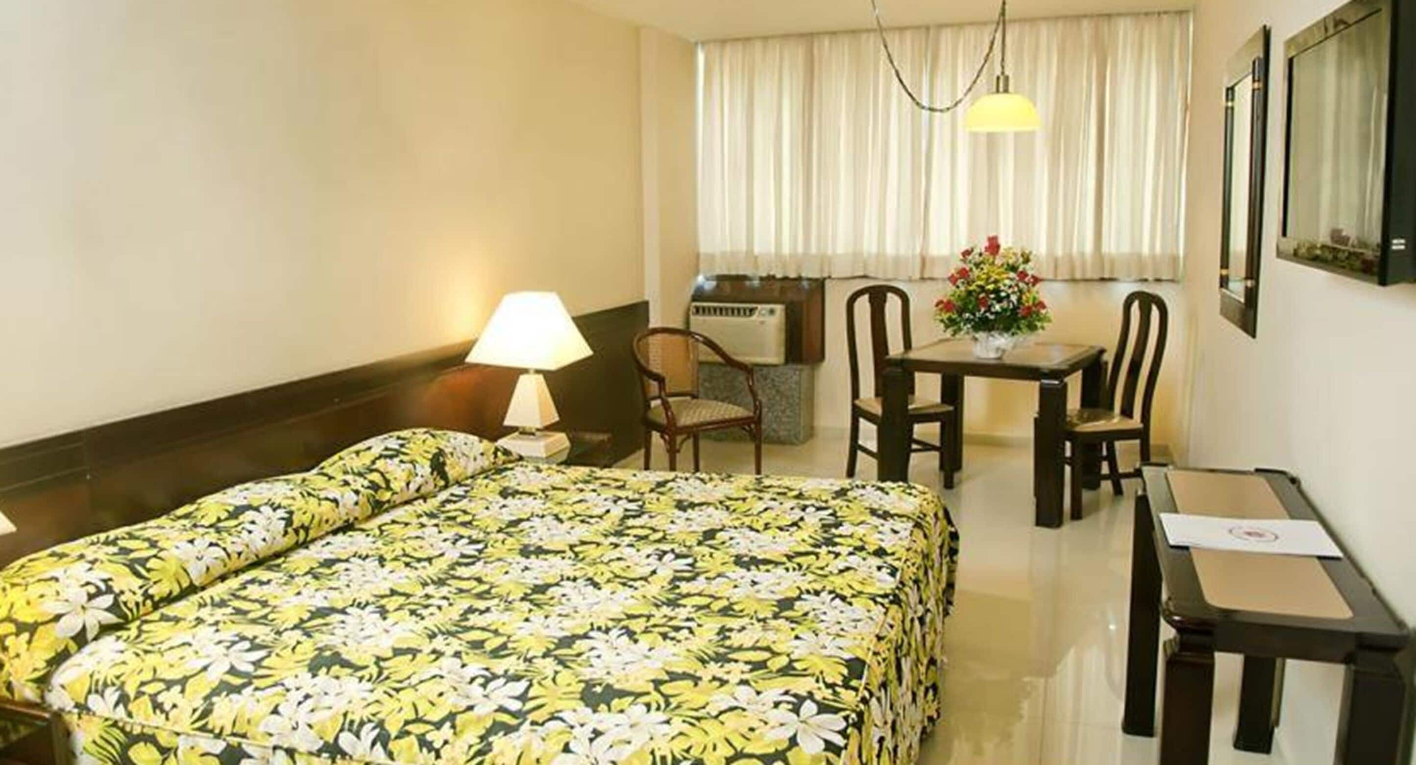 A hotel room with a bed, a desk, a chair, a lamp, and a window with curtains.