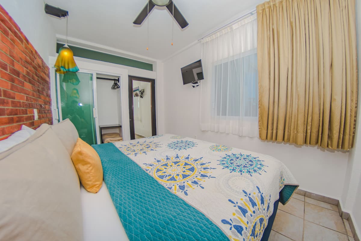 Ein Schlafzimmer mit Bett, einem Fenster mit Vorhängen, einem Deckenventilator und einem Fernseher an der Wand.