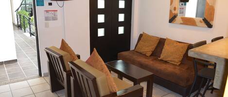 A room with a sofa, chairs, a small table, a TV mounted on the wall, and a mirror with a cow print frame.