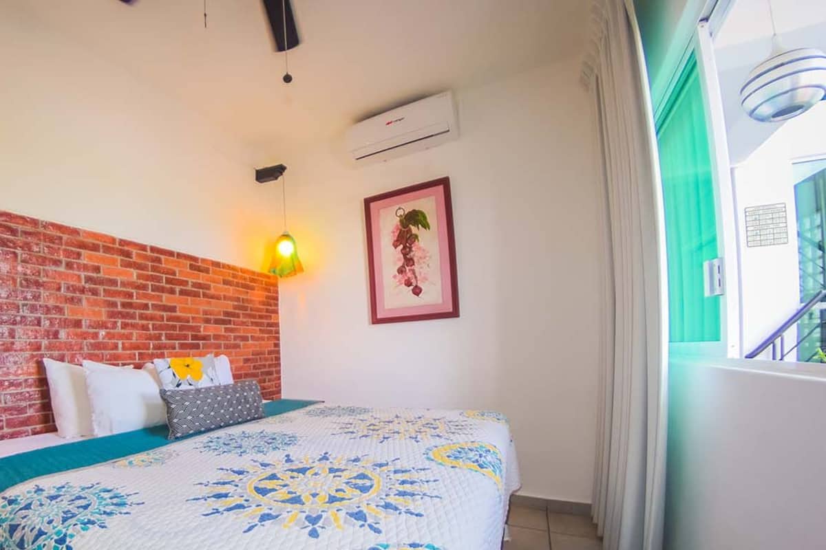 Ein Zimmer mit Backsteinwand, einem Bett mit gemustertem Überwurf, einer hängenden Leuchte und einem gerahmten Bild an der Wand.