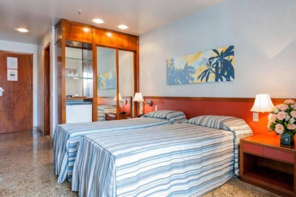 Une chambre d’hôtel avec un lit, des tables de chevet, un miroir et un tableau au mur.