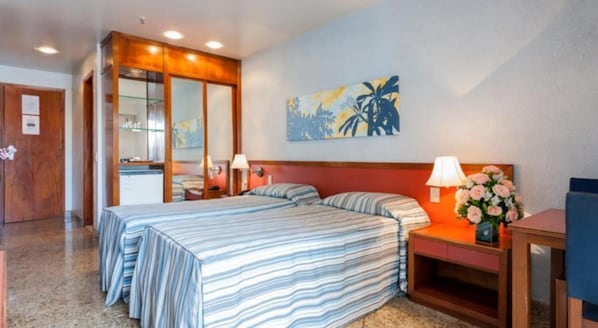 A hotel room with a bed, bedside tables, a mirror, and a painting on the wall.