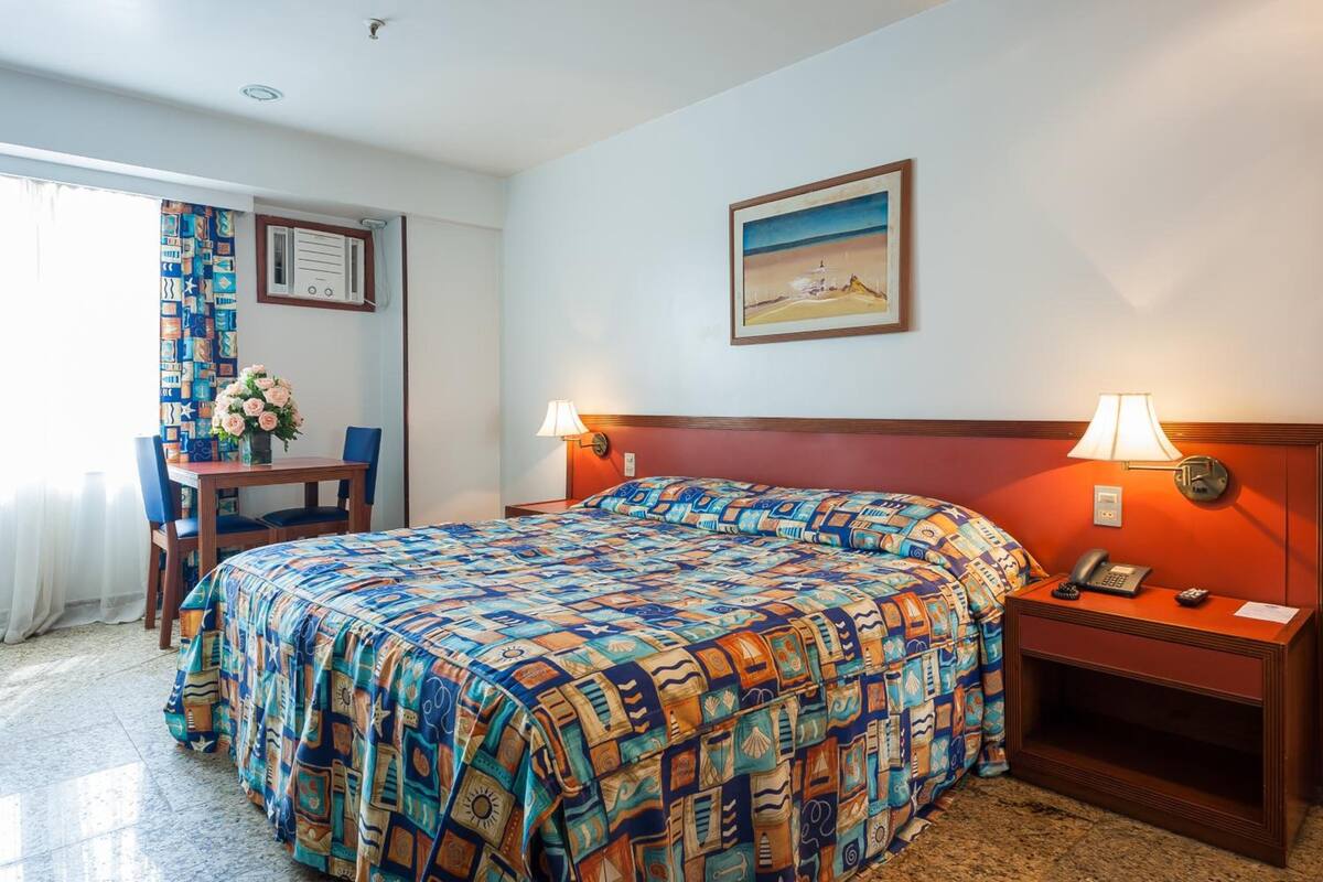 Une chambre d’hôtel avec un lit, un bureau et une chaise, un téléphone et un tableau au mur.