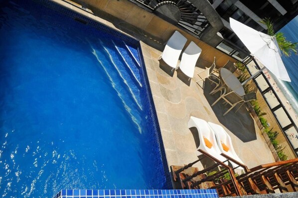 Una piscina con agua azul cristalina, rodeada de sillones de descanso y sombrillas.