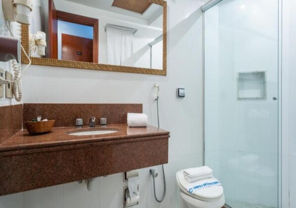 Un baño con encimera de granito, espejo, inodoro y cabina de ducha de vidrio.