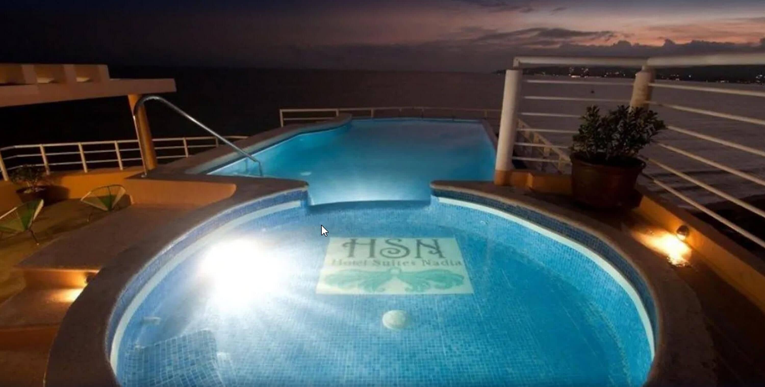 A pool area with a sign reading "HSN Hotel Suites Nadia" on a cruise ship deck at night.