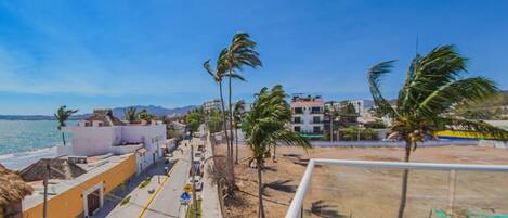 A coastal hotel with a view of the sea, palm trees, and a clear sky.