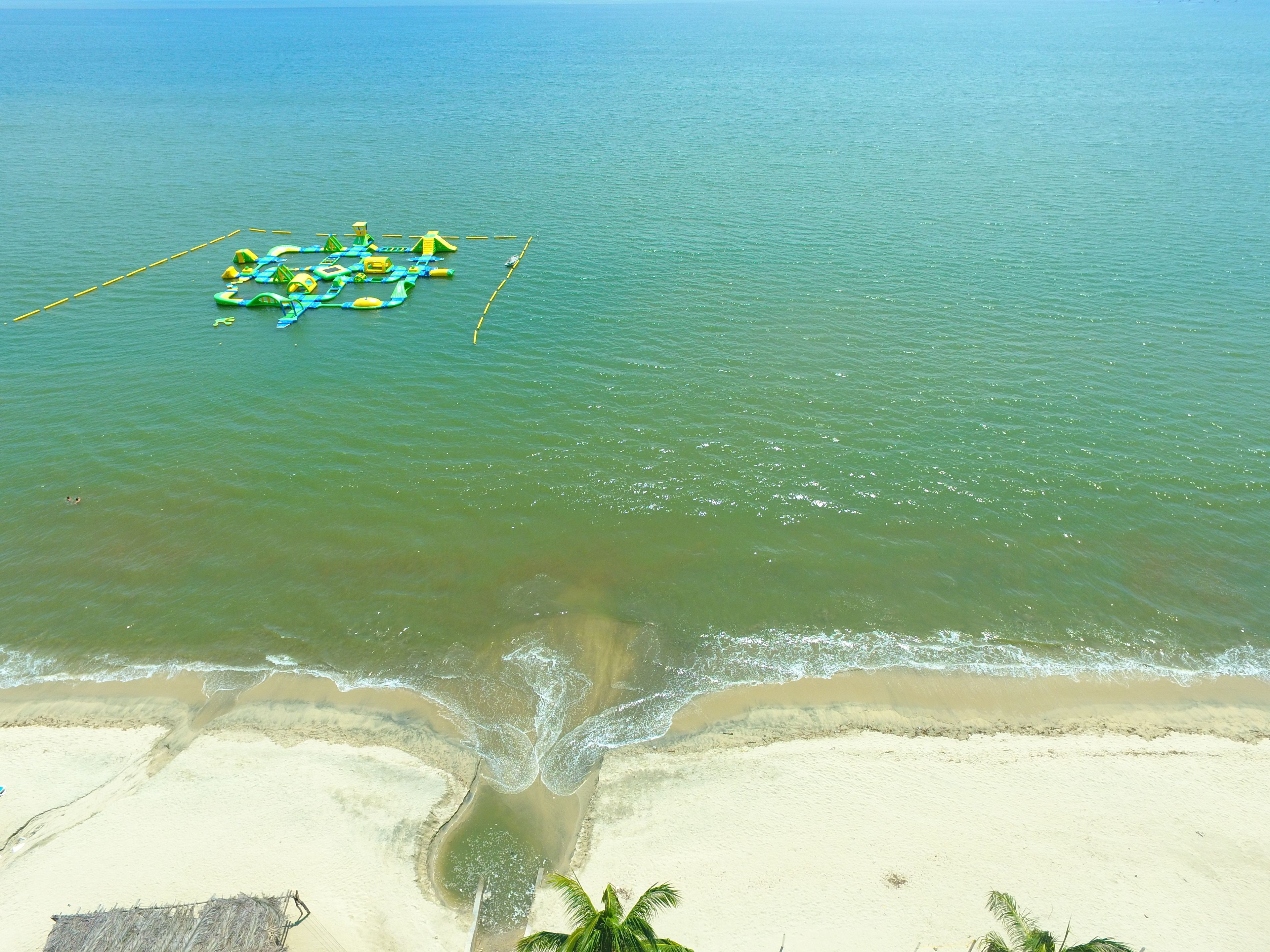 A beach with clear water and a floating structure with green and yellow elements.