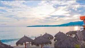 A beach with thatched umbrellas and a building with a balcony. - Hotel Boutique Suites Nadia Bucerias (Bucerías)