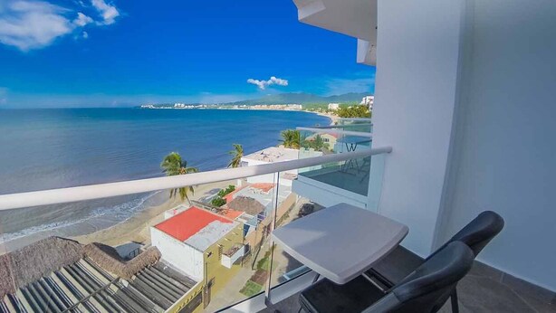 A balcony with a view of the ocean and beach, a small table, and a chair. - Hotel Boutique Suites Nadia Bucerias (Bucerías)