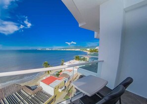 Un balcón con vista al océano y la playa, una mesita y una silla.