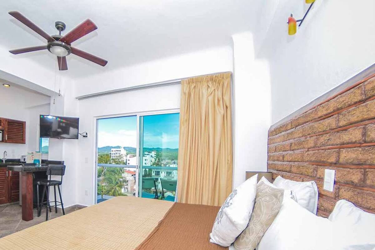 A hotel room with a bed, a desk, a television, and a view of the city.
