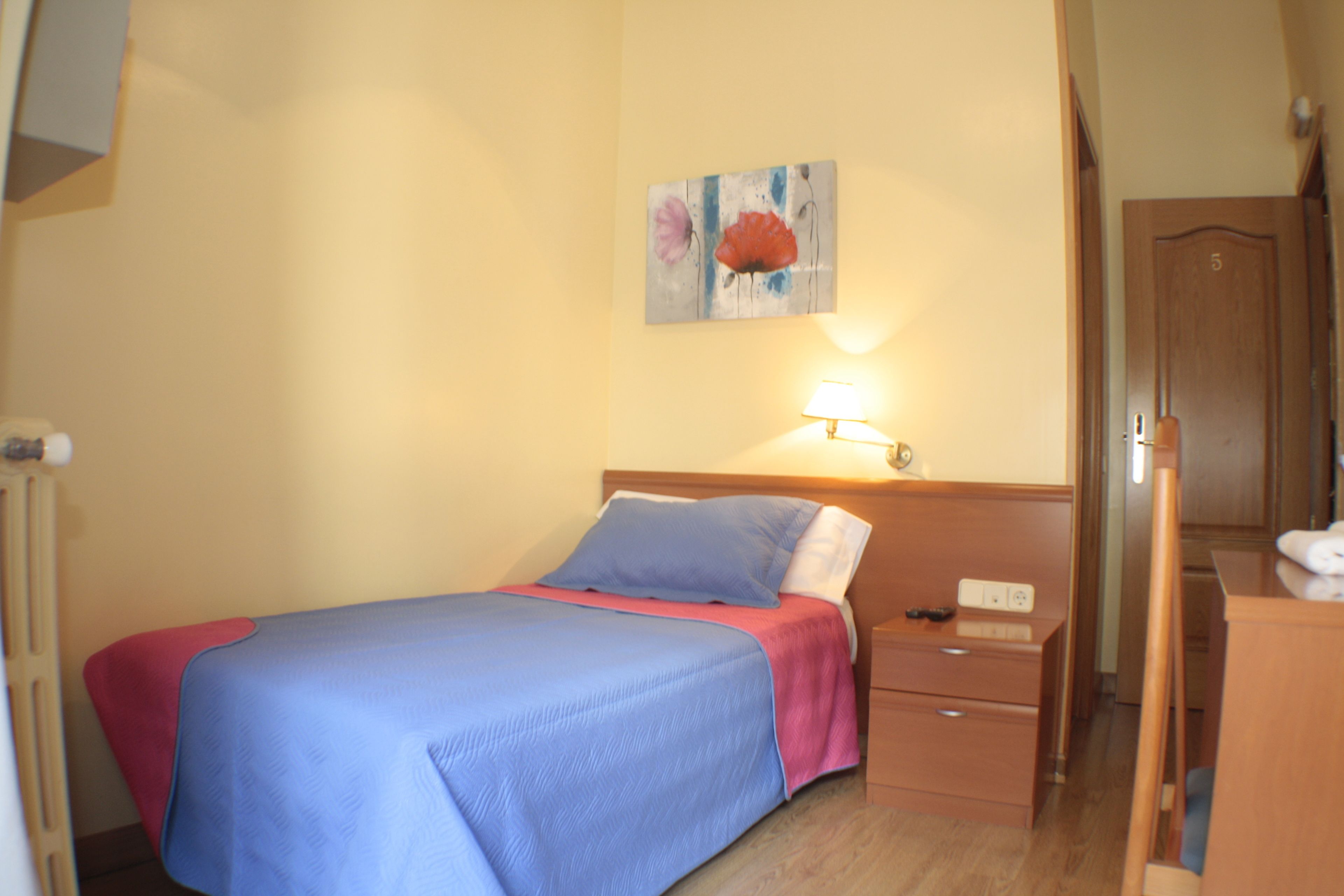 A bedroom with a bed, bedside table, lamp, and a door.
