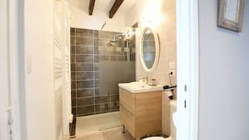A modern bathroom with a glass-enclosed shower, a wooden vanity, and a round mirror.