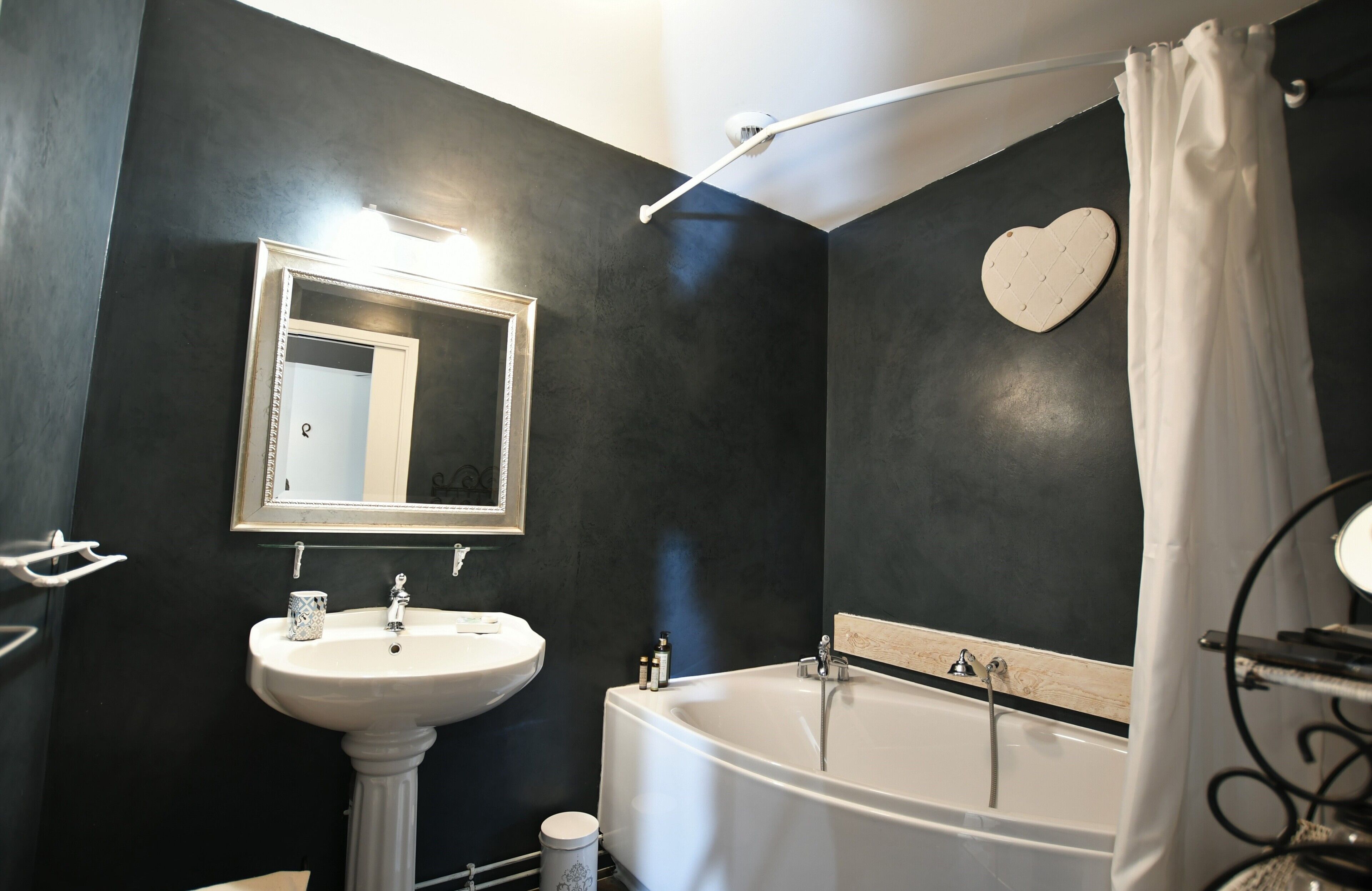 A bathroom with a white sink, a bathtub, a heart-shaped mirror, and a shower curtain.