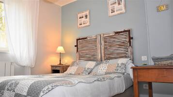 Un dormitorio con una cama, una mesita de noche con lámpara, una mesita auxiliar con cesta y una pared con un letrero que dice 'HOME'.