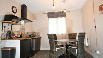 A compact kitchen with a microwave, stove, and sink. There is a dining table with wicker chairs and a window with curtains.