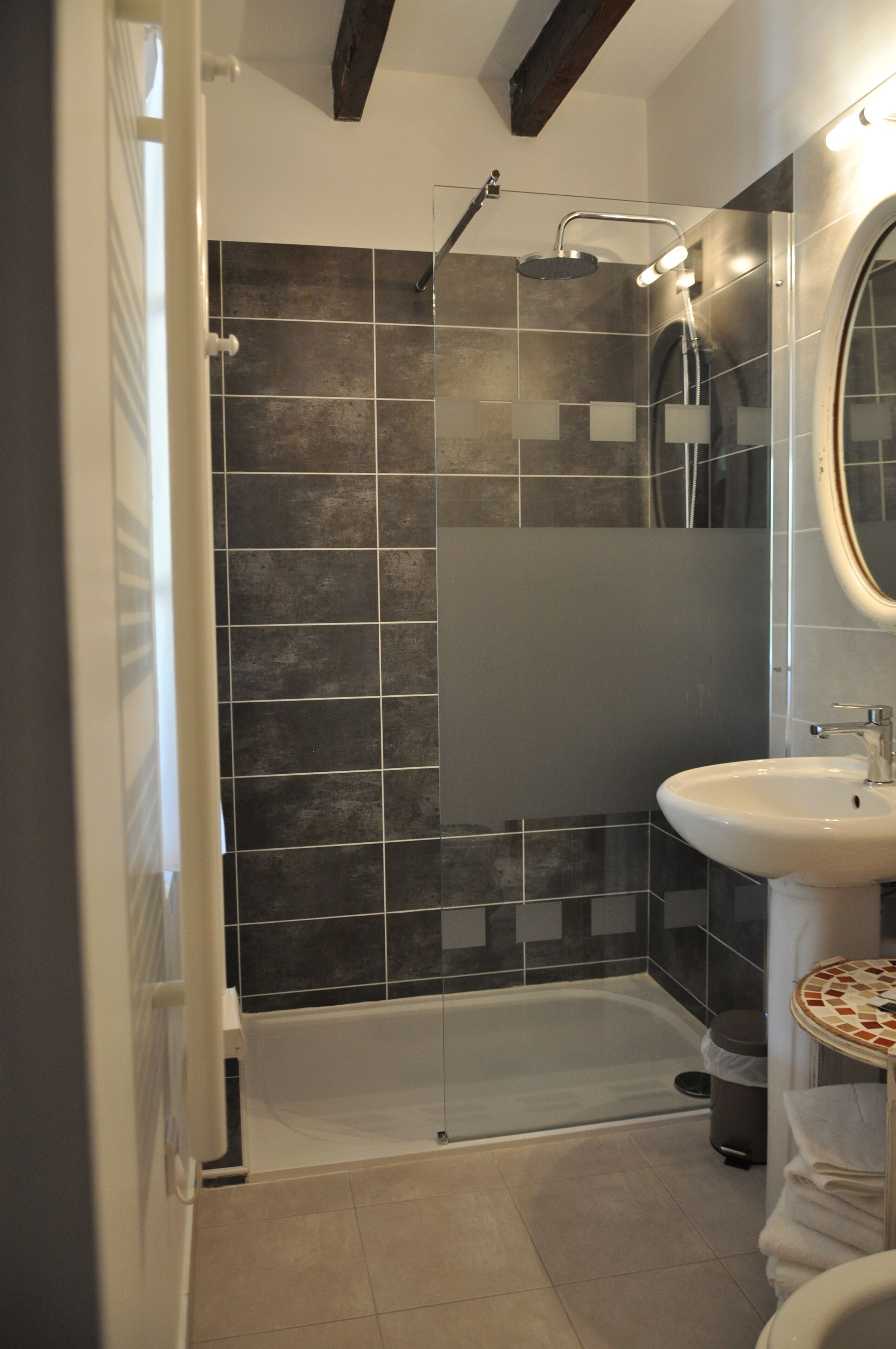 A modern bathroom with a glass-enclosed shower, a white sink, and a tiled floor.