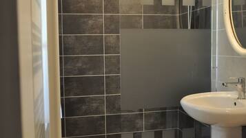 A modern bathroom with a glass-enclosed shower, a white sink, and a tiled floor.