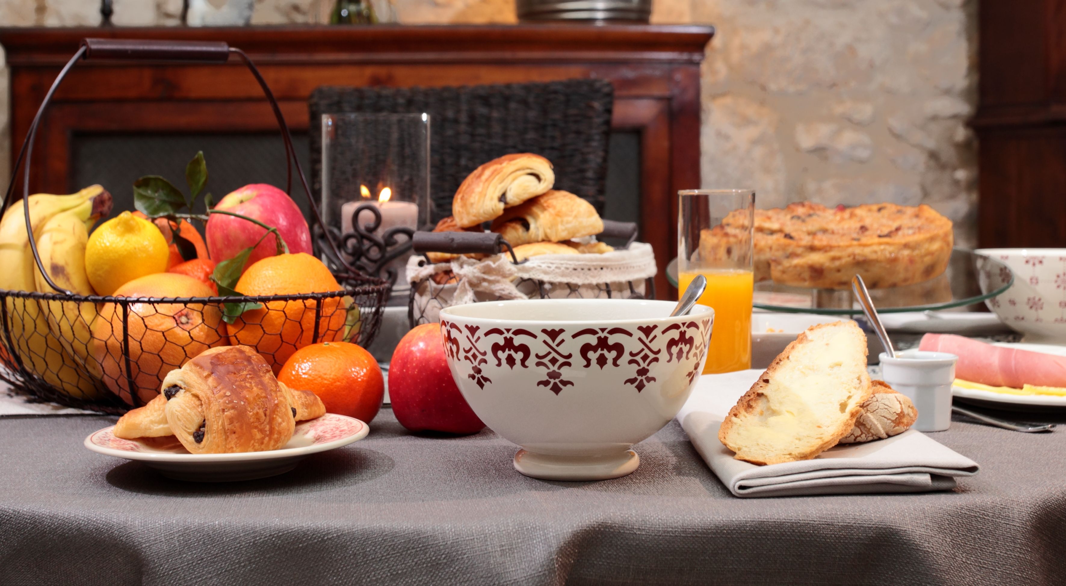 A breakfast setting with fruits, pastries, and a glass of orange juice on a table.