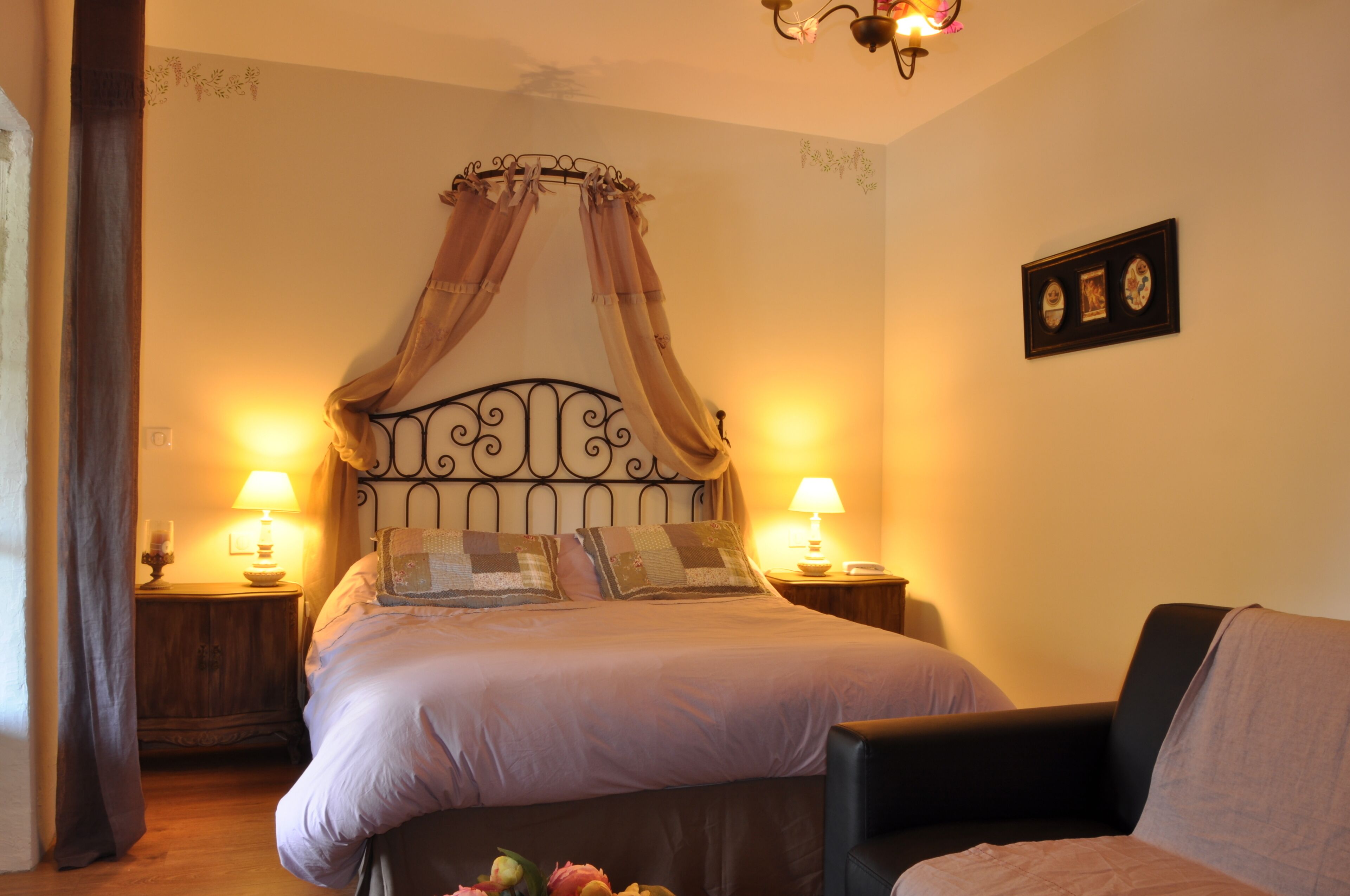 A bedroom with a four-poster bed, two bedside lamps, a framed picture on the wall, and a chair in the corner.