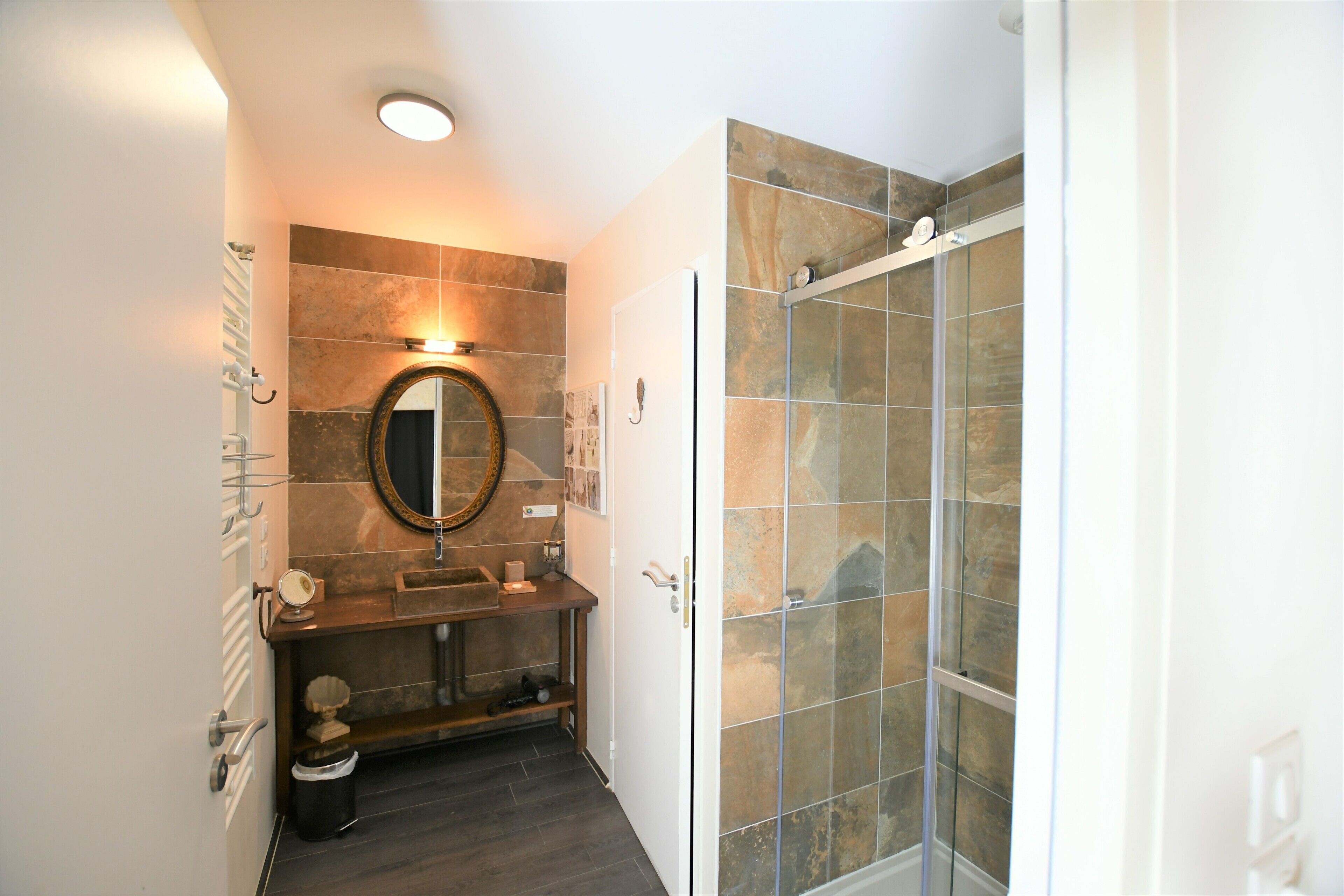 A bathroom with a stone-tiled shower, a sink with a mirror, and a wooden vanity.