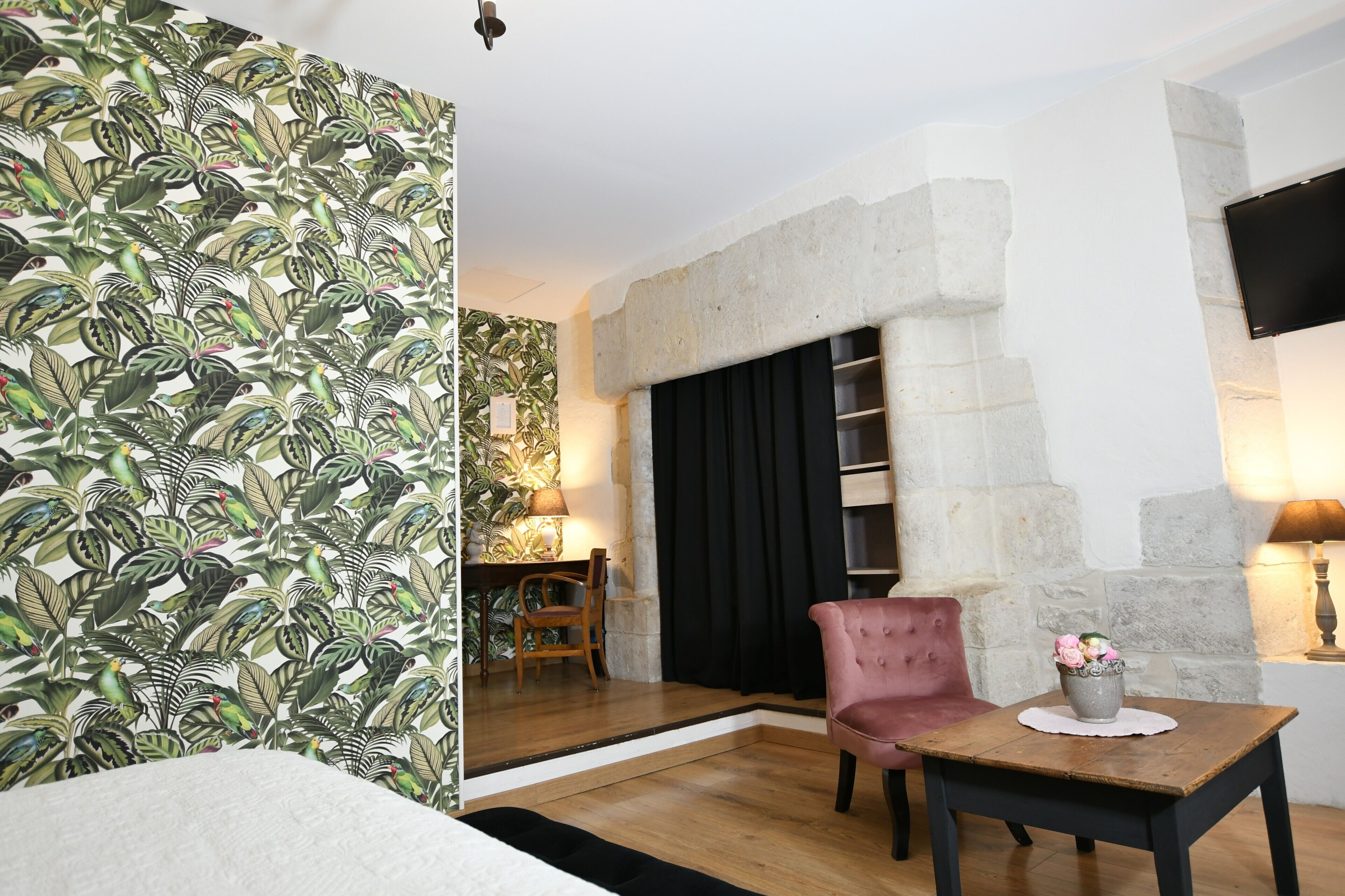 A room with a stone fireplace, a wooden table with a vase of flowers, and a patterned wallpaper.