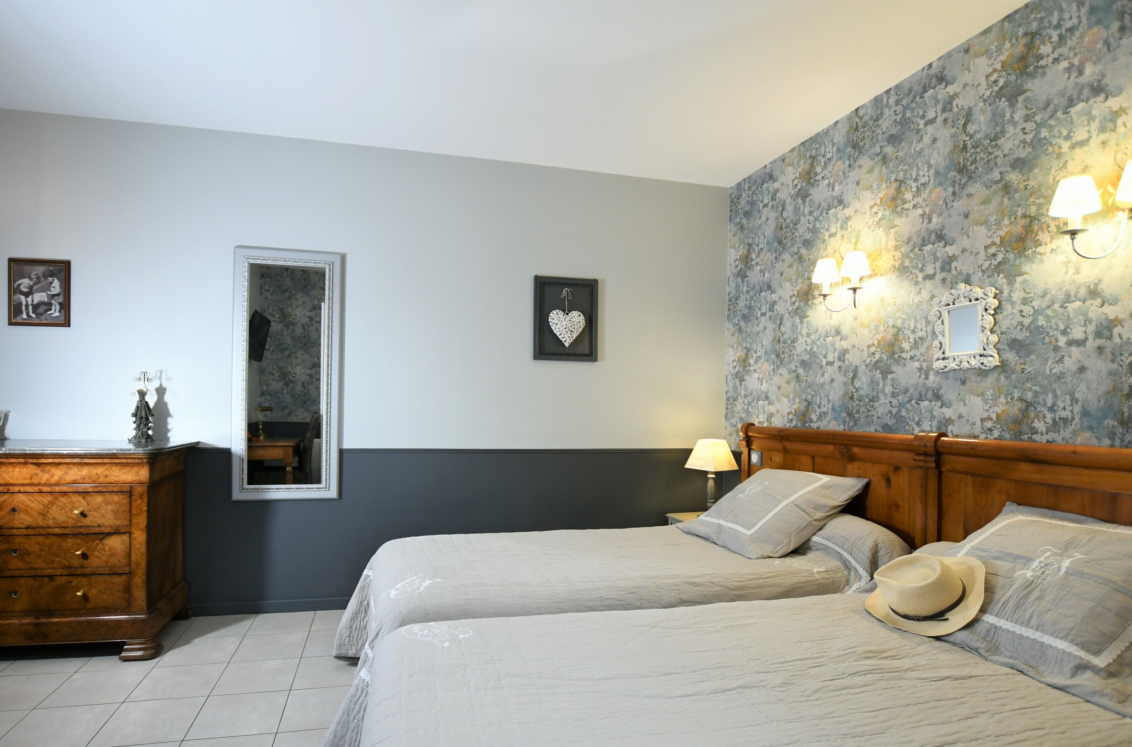 Une chambre avec deux lits, une commode, un miroir et des lampes fixées au mur.