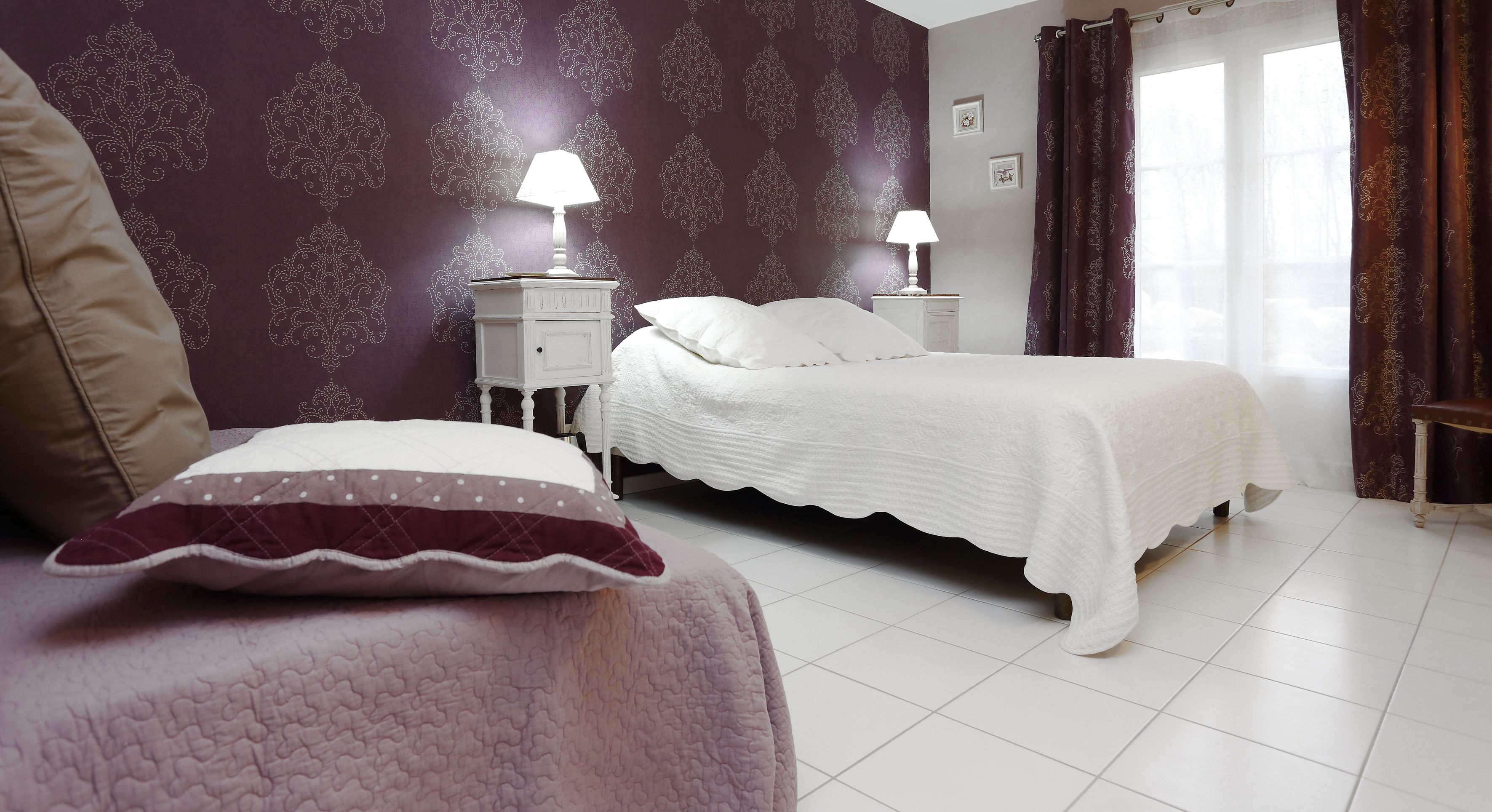 Une chambre à coucher avec un lit, deux tables de chevet avec des lampes, une fenêtre avec des rideaux et un mur à motifs.
