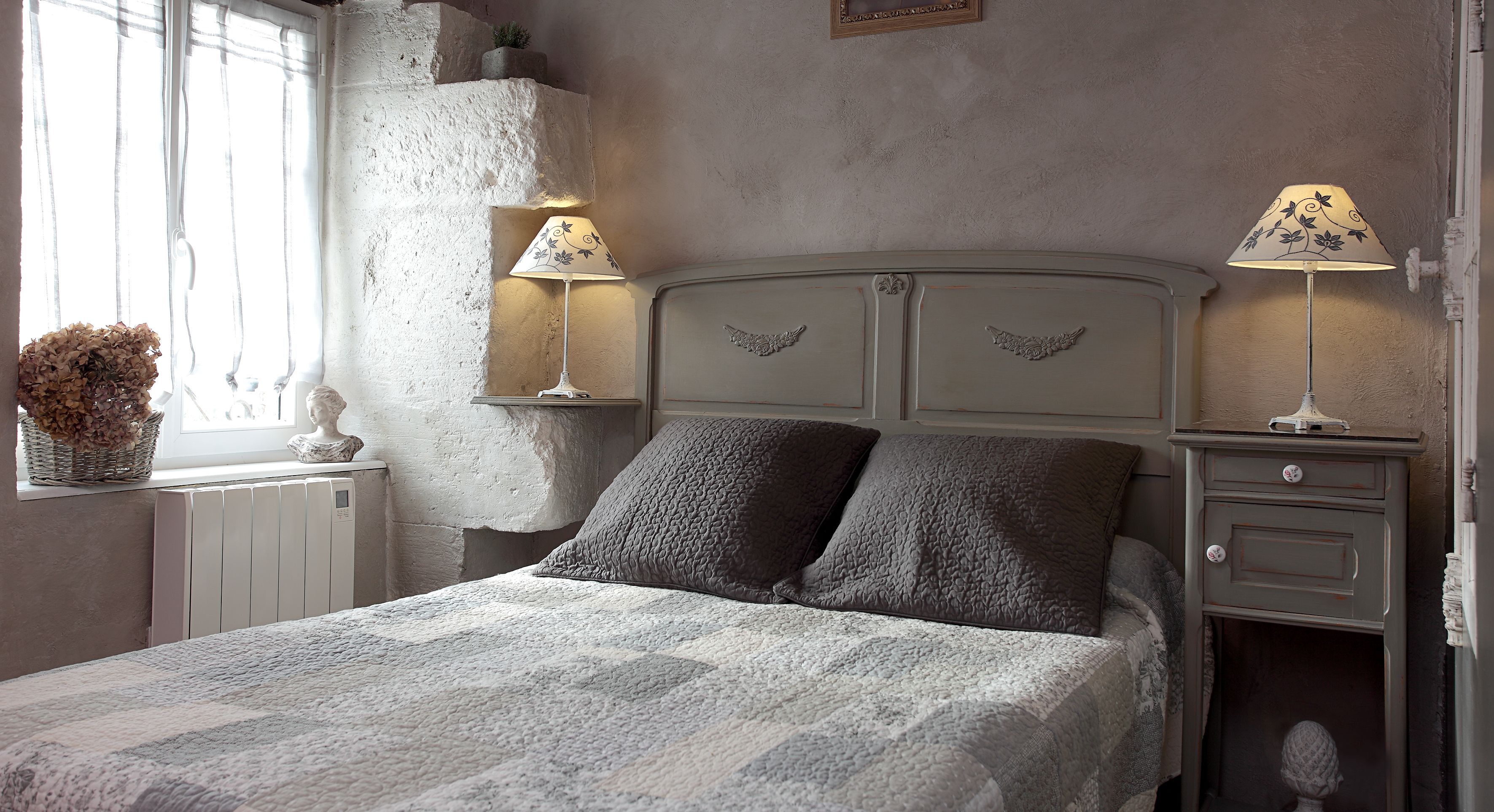 A bedroom with a bed, two bedside lamps, a nightstand, a dresser, a window with a view, and a decorative basket.
