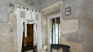 A room with stone walls, a wooden bench, a black sofa with patterned cushions, and a white canopy bed. - Le Mas des Bories - Grand Périgueux (Antonne-et-Trigonant)